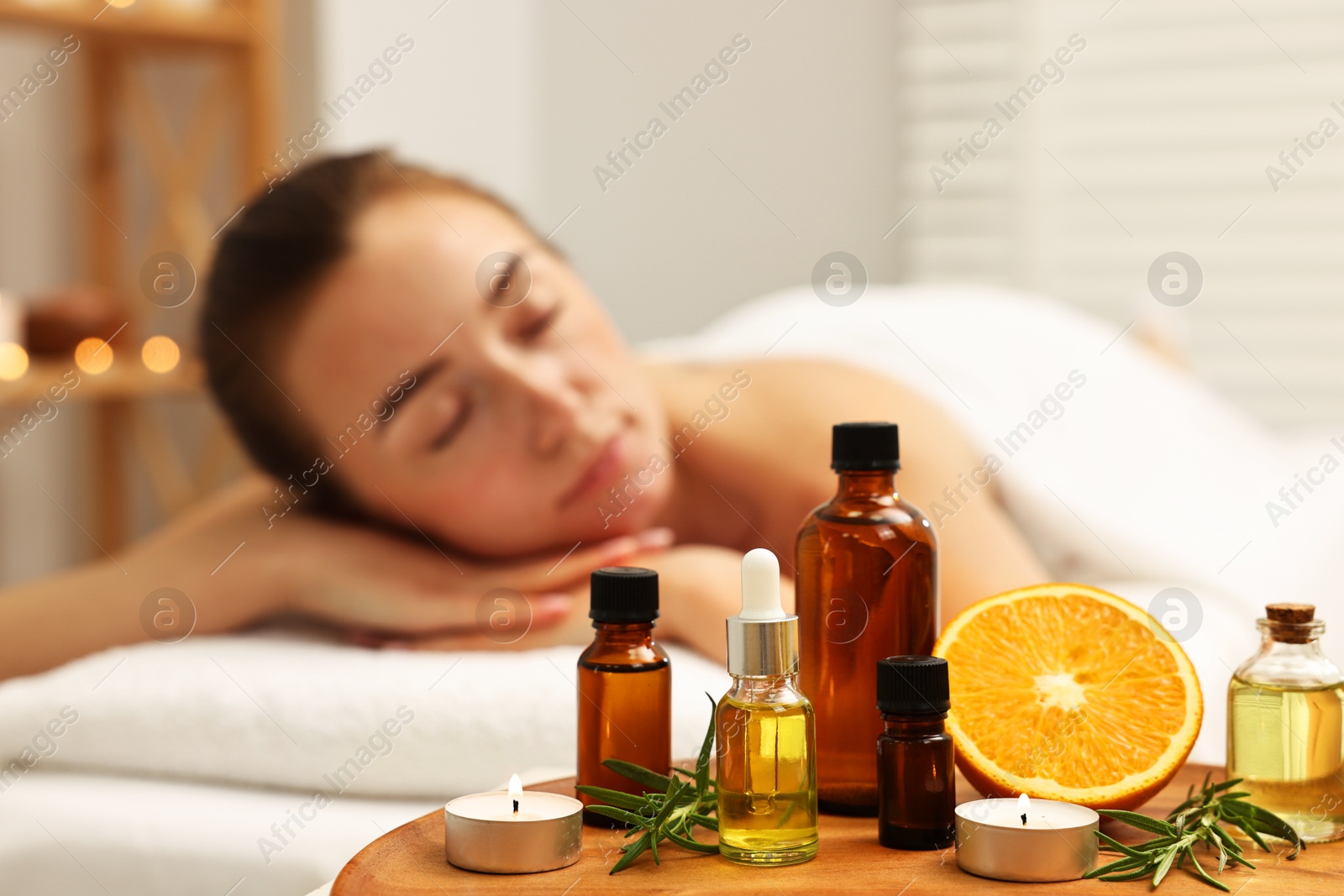 Photo of Aromatherapy. Woman relaxing on massage couch in spa salon, focus on bottles of essential oils and other aromatic products