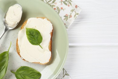 Delicious sandwich with cream cheese and basil leaves on white wooden table, top view. Space for text