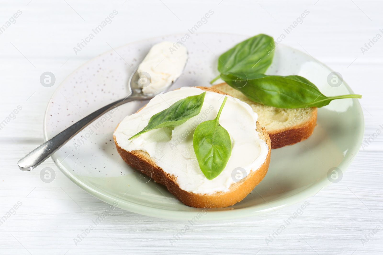 Photo of Pieces of bread with cream cheese and basil leaves on white wooden table