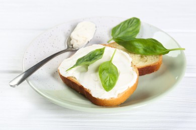 Photo of Pieces of bread with cream cheese and basil leaves on white wooden table