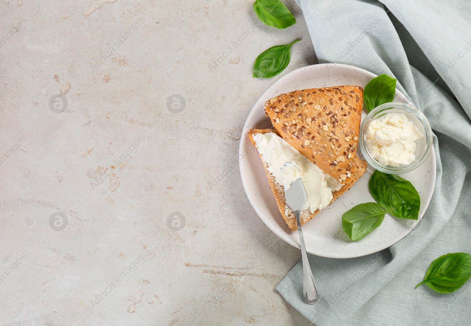 Photo of Pieces of bread with cream cheese and basil leaves on light gray textured table, top view. Space for text