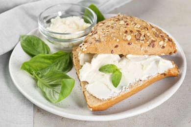 Pieces of bread with cream cheese and basil leaves on light gray table, closeup