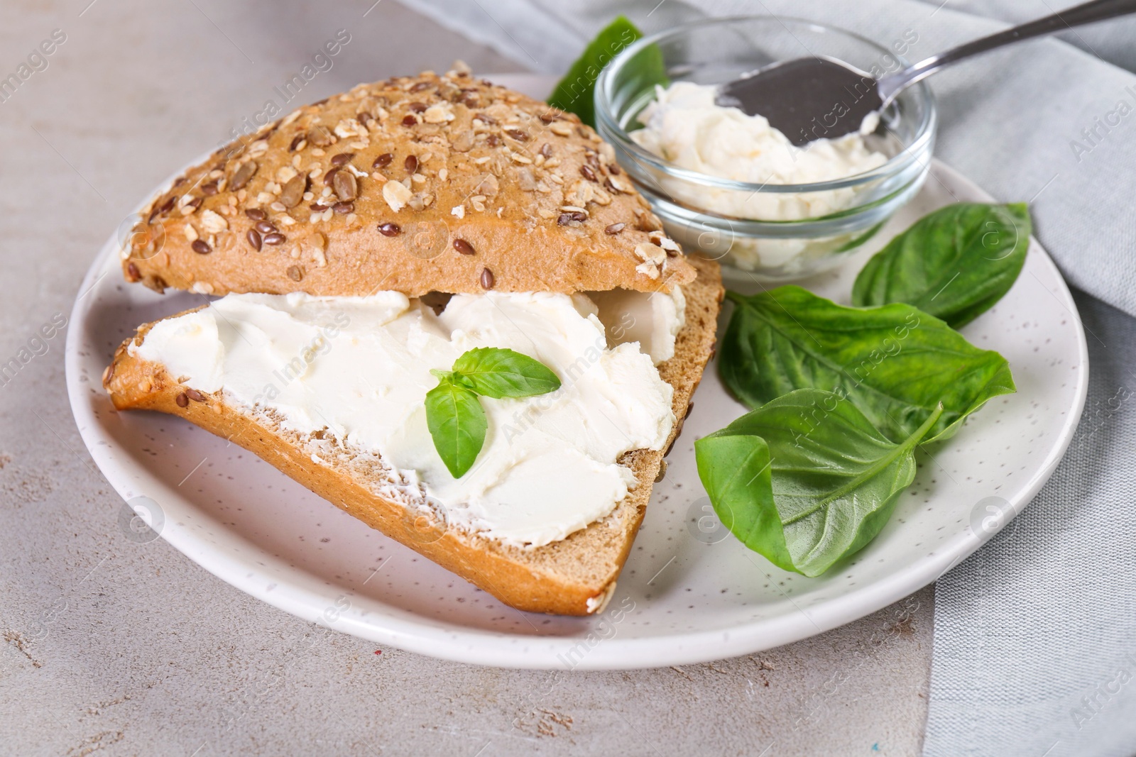 Photo of Pieces of bread with cream cheese and basil leaves on light gray textured table, closeup