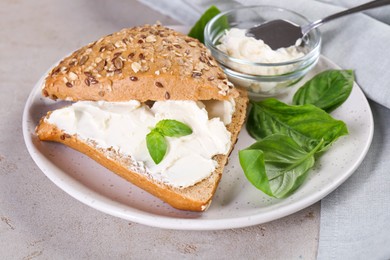 Photo of Pieces of bread with cream cheese and basil leaves on light gray textured table, closeup