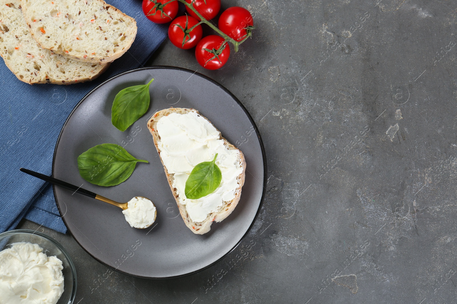 Photo of Pieces of bread with cream cheese, basil leaves and tomatoes on gray textured table, flat lay. Space for text