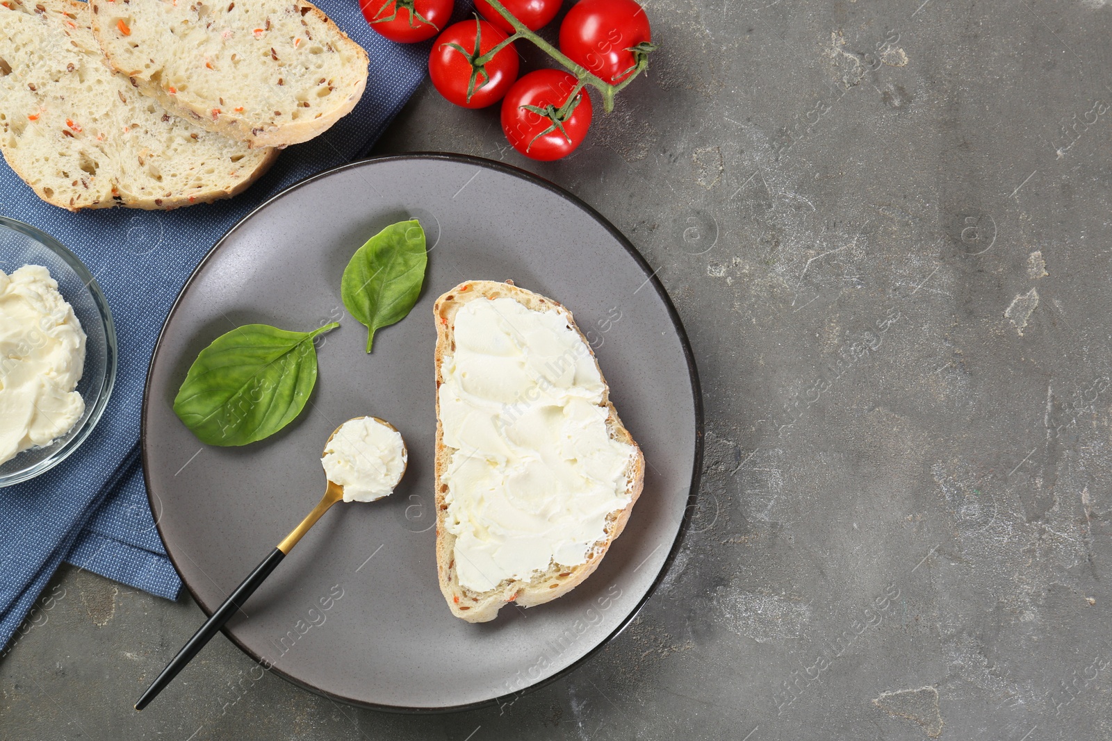 Photo of Pieces of bread with cream cheese, basil leaves and tomatoes on gray textured table, flat lay. Space for text