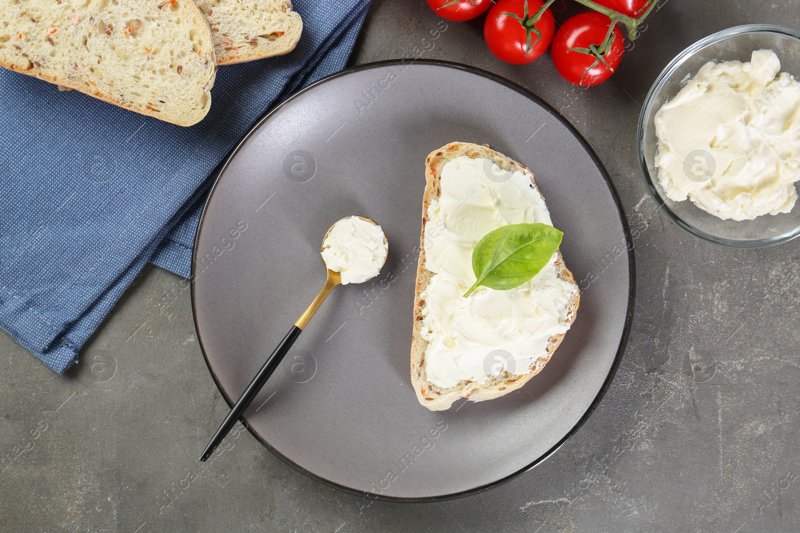 Photo of Pieces of bread with cream cheese, basil leaves and tomatoes on gray textured table, flat lay