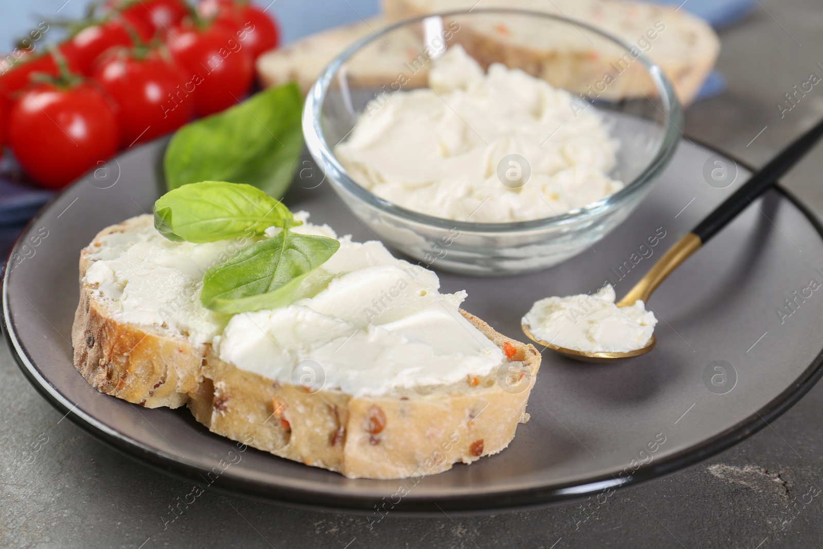 Photo of Piece of bread with cream cheese and basil leaves on gray table, closeup