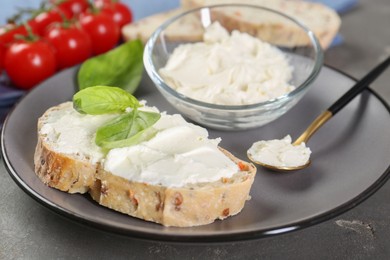 Piece of bread with cream cheese and basil leaves on gray table, closeup