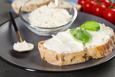 Photo of Piece of bread with cream cheese and basil leaves on gray table, closeup