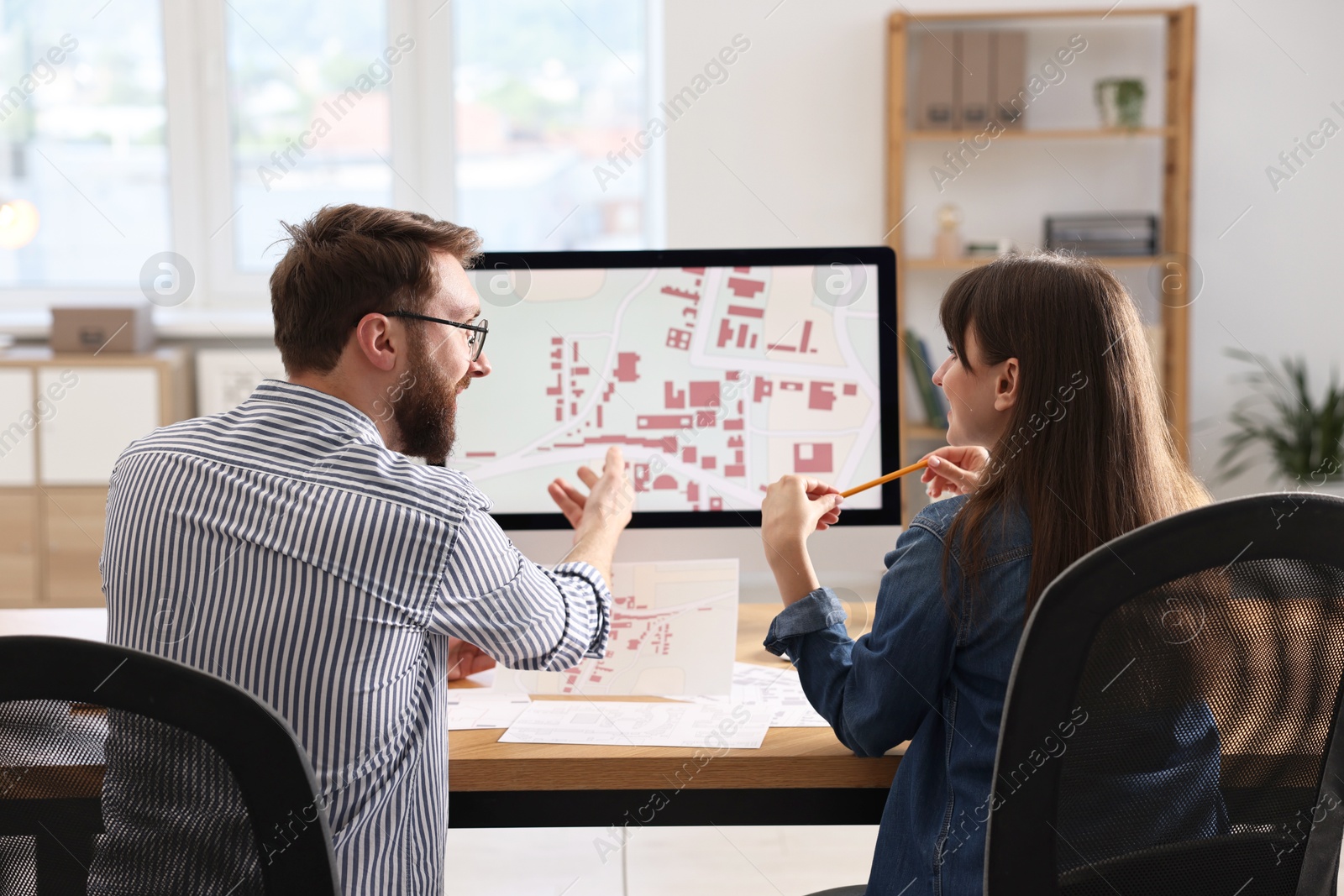 Photo of Cartographers working with cadastral maps at table in office, back view