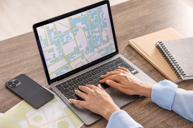 Cartographer working with cadastral map on laptop at wooden table in office, closeup