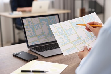 Photo of Cartographer working with cadastral maps at wooden table in office, closeup