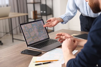 Cartographers working with cadastral map on laptop at wooden table in office, closeup