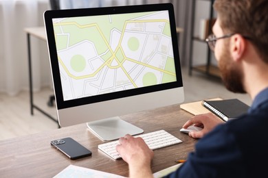 Photo of Cartographer working with cadastral map on computer at wooden table in office, closeup