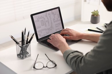 Cartographer working with cadastral map on laptop at white table in office, closeup