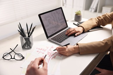 Cartographers working with cadastral maps at white table in office, closeup