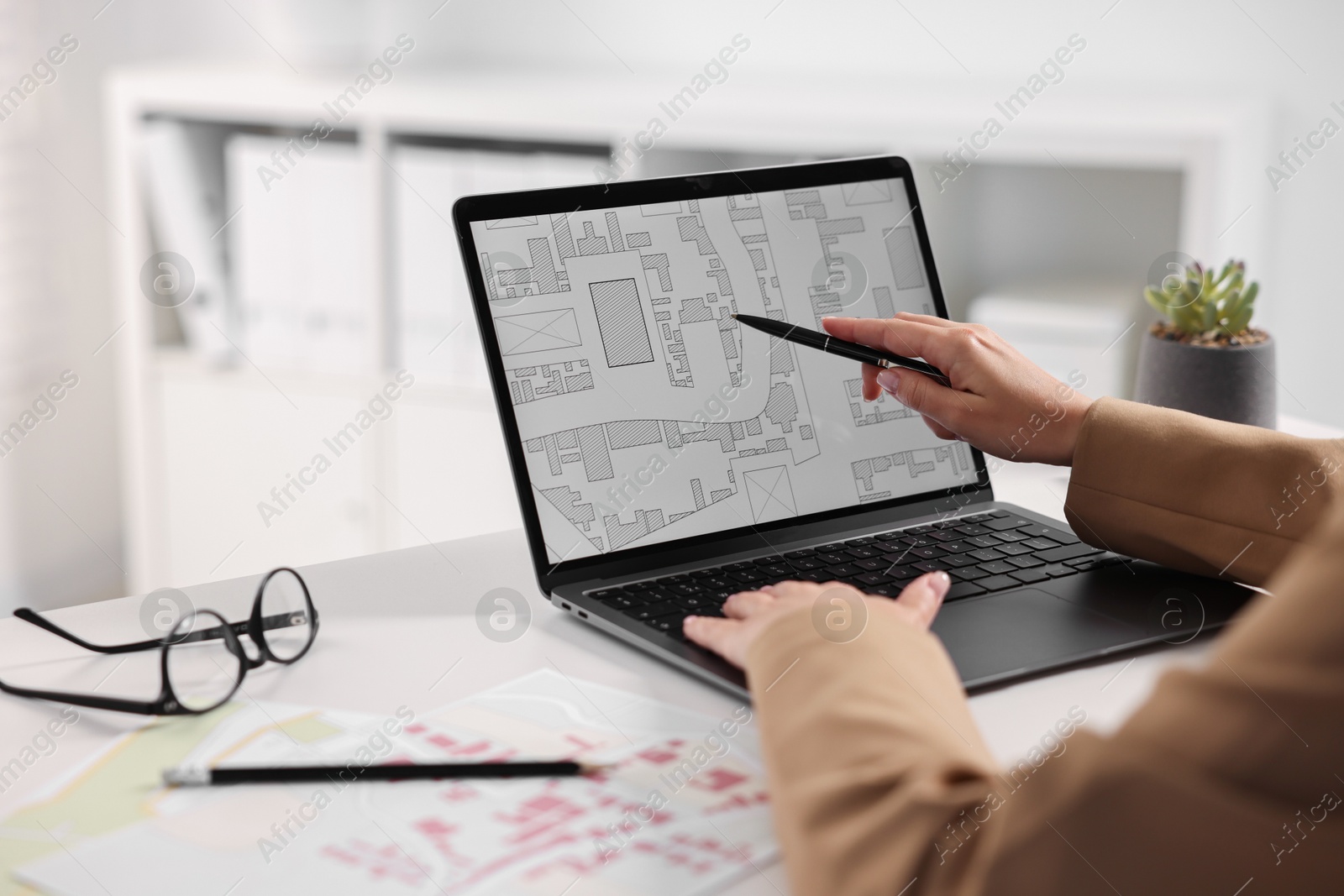 Photo of Cartographer working with cadastral map on laptop at white table in office, closeup