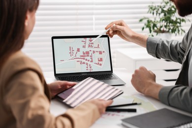 Cartographers working with cadastral map on laptop at white table in office, closeup