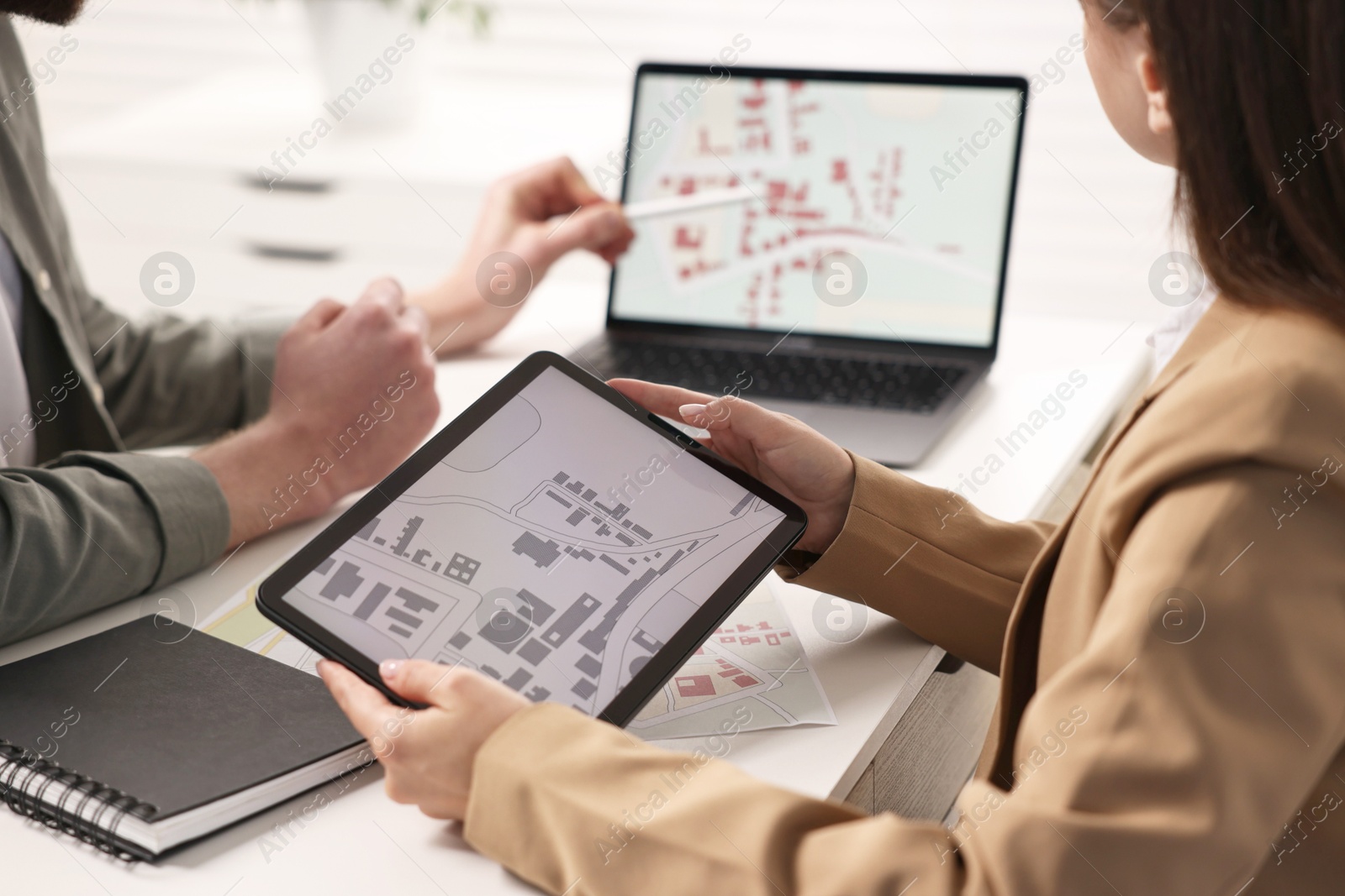 Photo of Cartographers working with cadastral maps at white table in office, closeup