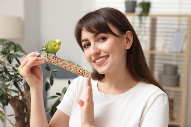 Woman feeding bright parrot with bird treat indoors. Exotic pet