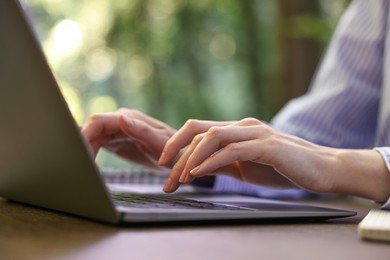 Photo of Businesswoman working with laptop at table outdoors, closeup. Remote job