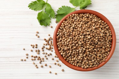 Dried coriander seeds in bowl and green leaves on wooden table, flat lay