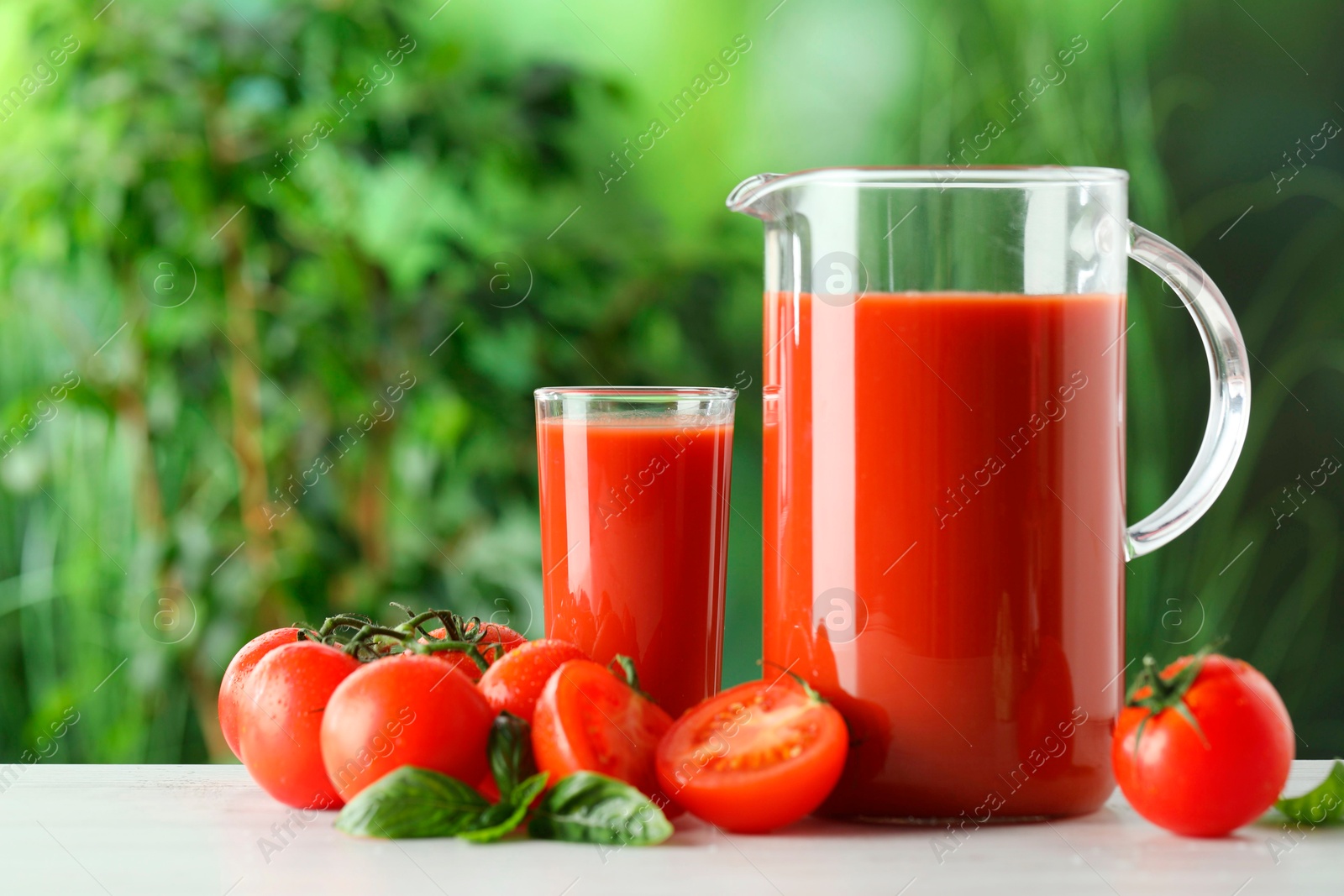 Photo of Tasty tomato juice, basil and fresh vegetables on white table outdoors