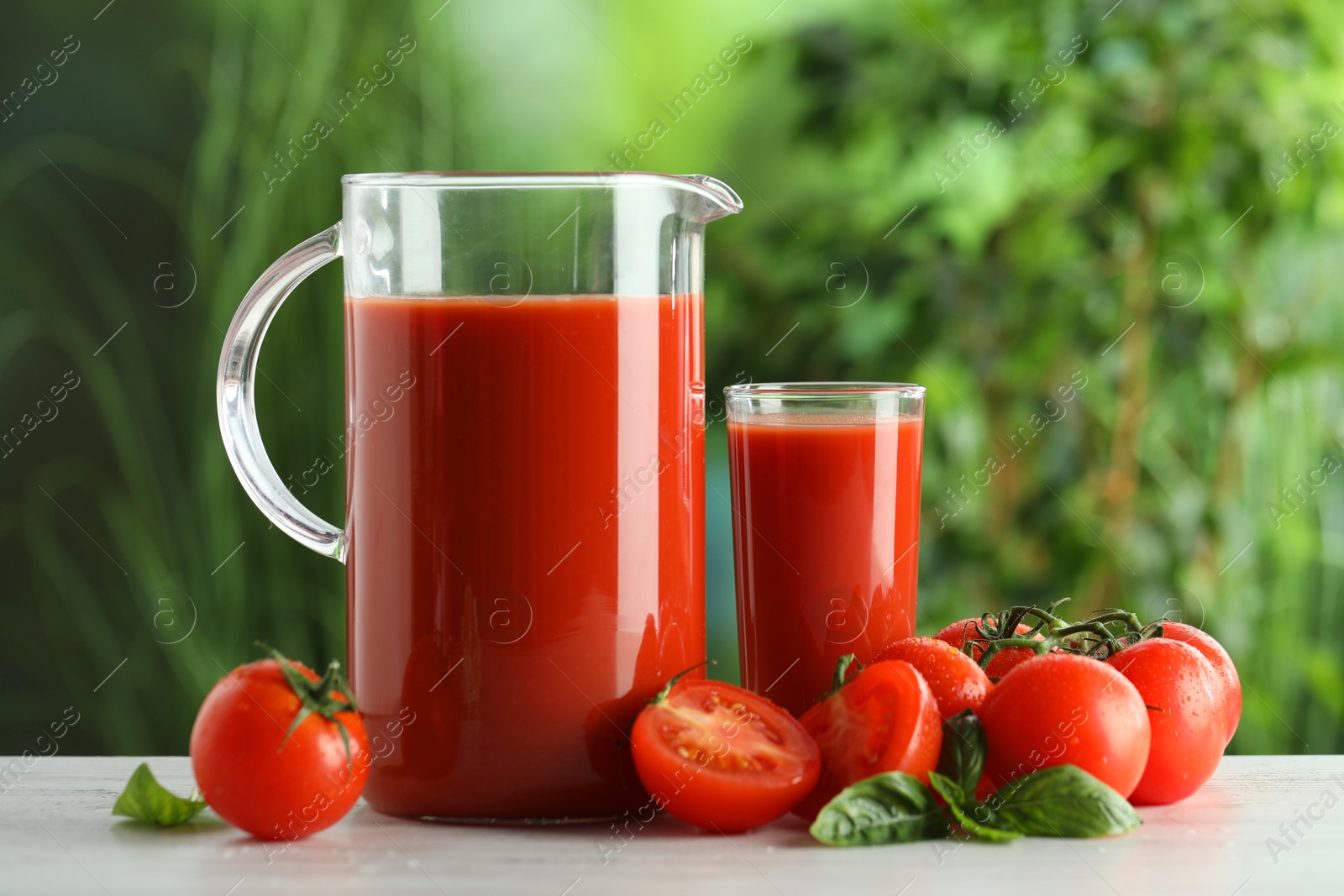 Photo of Tasty tomato juice, basil and fresh vegetables on white table outdoors