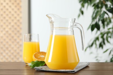 Tasty orange juice in jug, glass and citrus fruit on wooden table