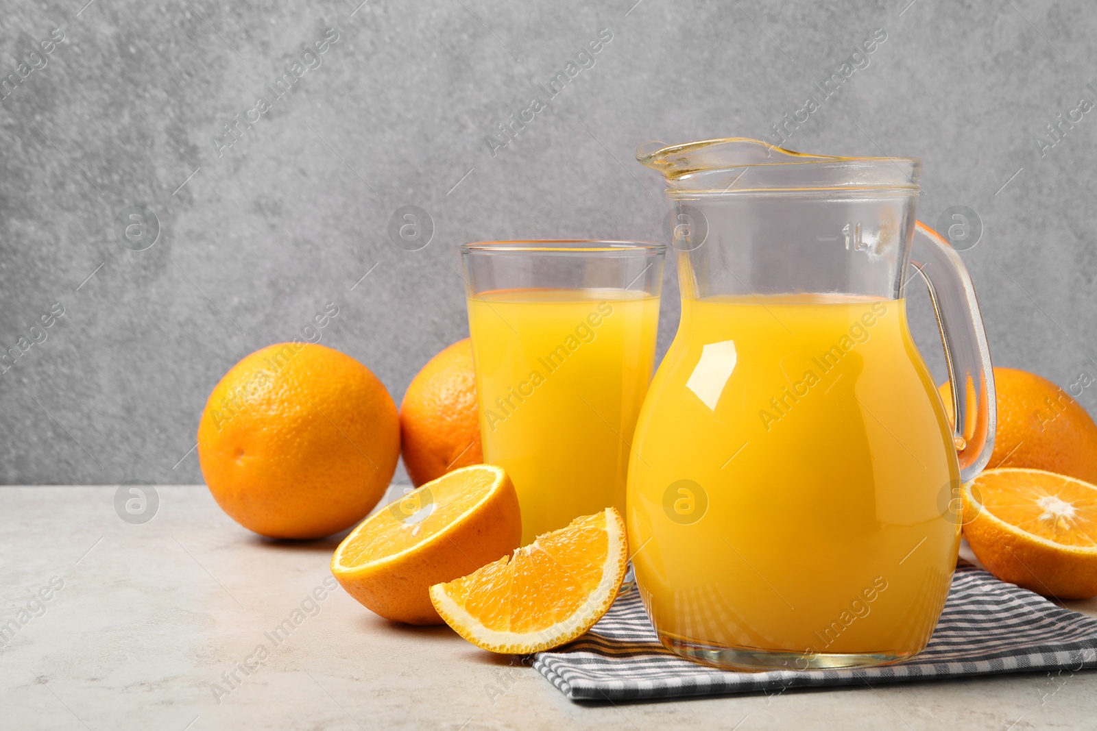 Photo of Tasty orange juice in jug, glass and citrus fruits on light table. Space for text