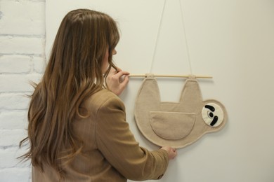 Photo of Woman hanging decorative toy sloth on wall, back view