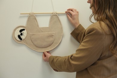 Photo of Woman hanging decorative toy sloth on wall, closeup