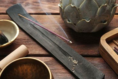 Photo of Incense stick smoldering in holder and Tibetan singing bowl on wooden table, closeup. Om ligature