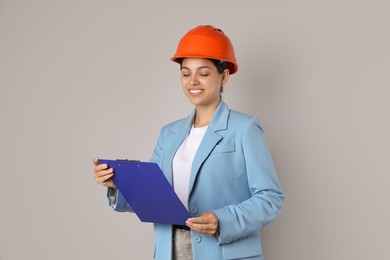 Engineer in hard hat with clipboard on grey background