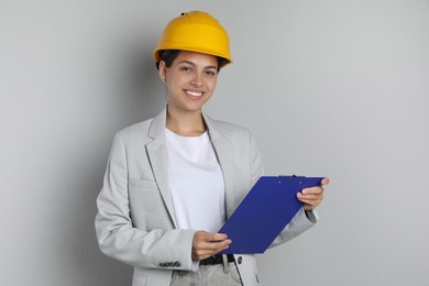 Photo of Engineer in hard hat with clipboard on grey background