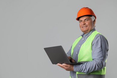 Engineer in hard hat with laptop on grey background, space for text