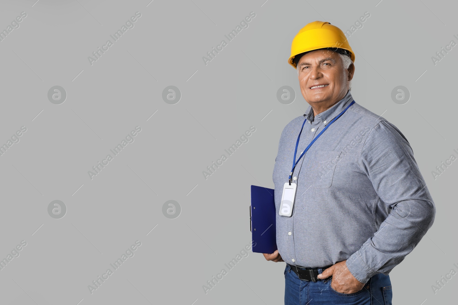 Photo of Engineer in hard hat with clipboard on grey background, space for text