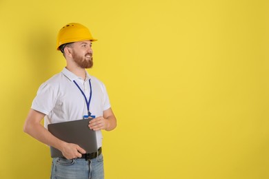 Photo of Engineer in hard hat with laptop on yellow background, space for text