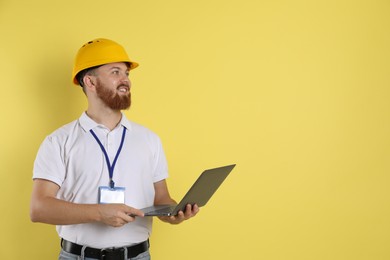 Photo of Engineer in hard hat with laptop on yellow background, space for text