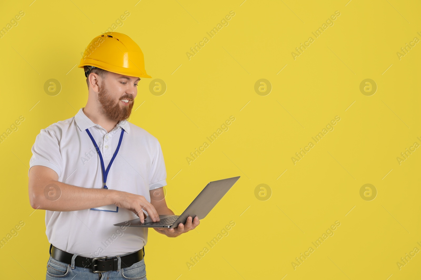 Photo of Engineer in hard hat with laptop on yellow background, space for text