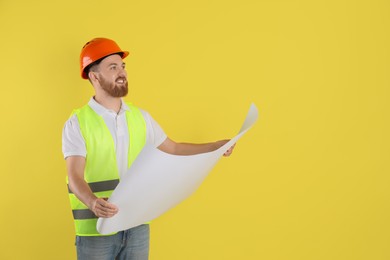 Engineer in hard hat with draft on yellow background, space for text