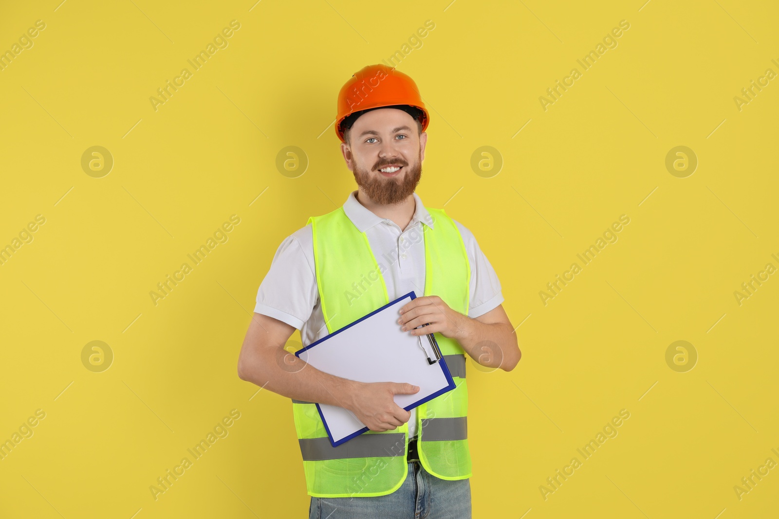 Photo of Engineer in hard hat with clipboard on yellow background