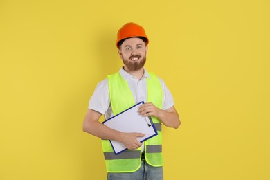 Engineer in hard hat with clipboard on yellow background