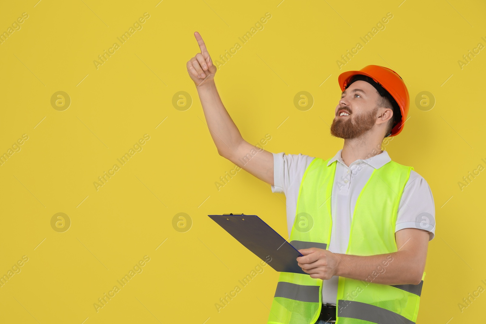 Photo of Engineer in hard hat with clipboard on yellow background, space for text