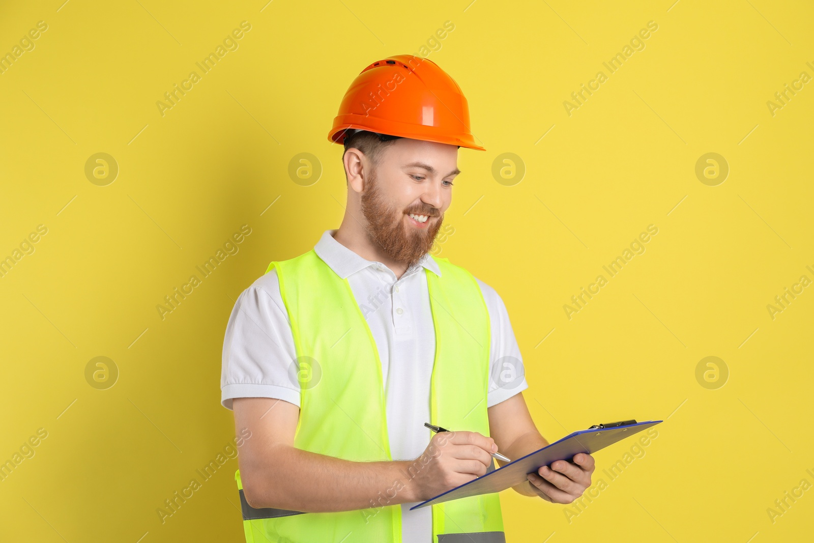 Photo of Engineer in hard hat with clipboard and pen on yellow background