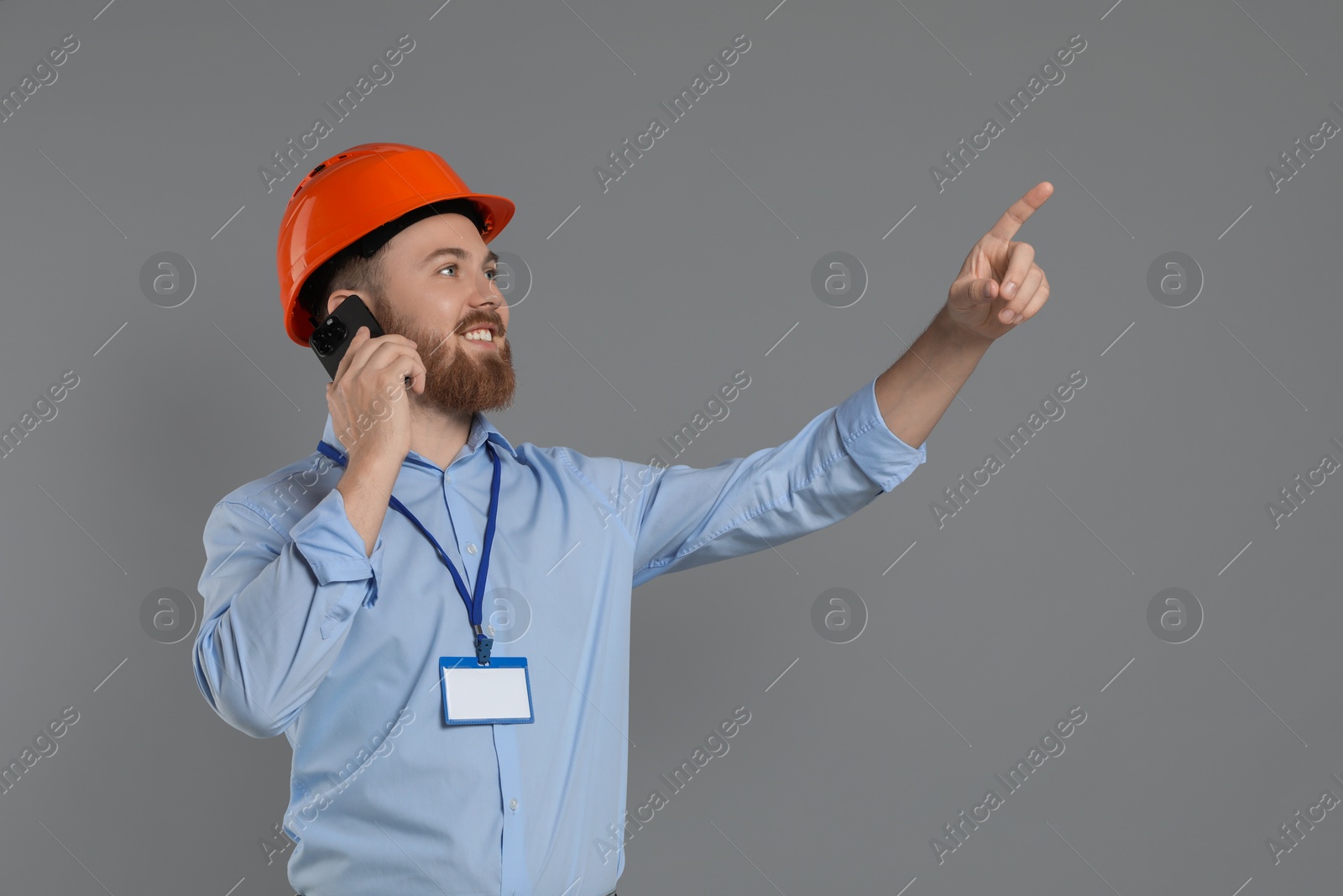 Photo of Engineer in hard hat talking on smartphone against grey background