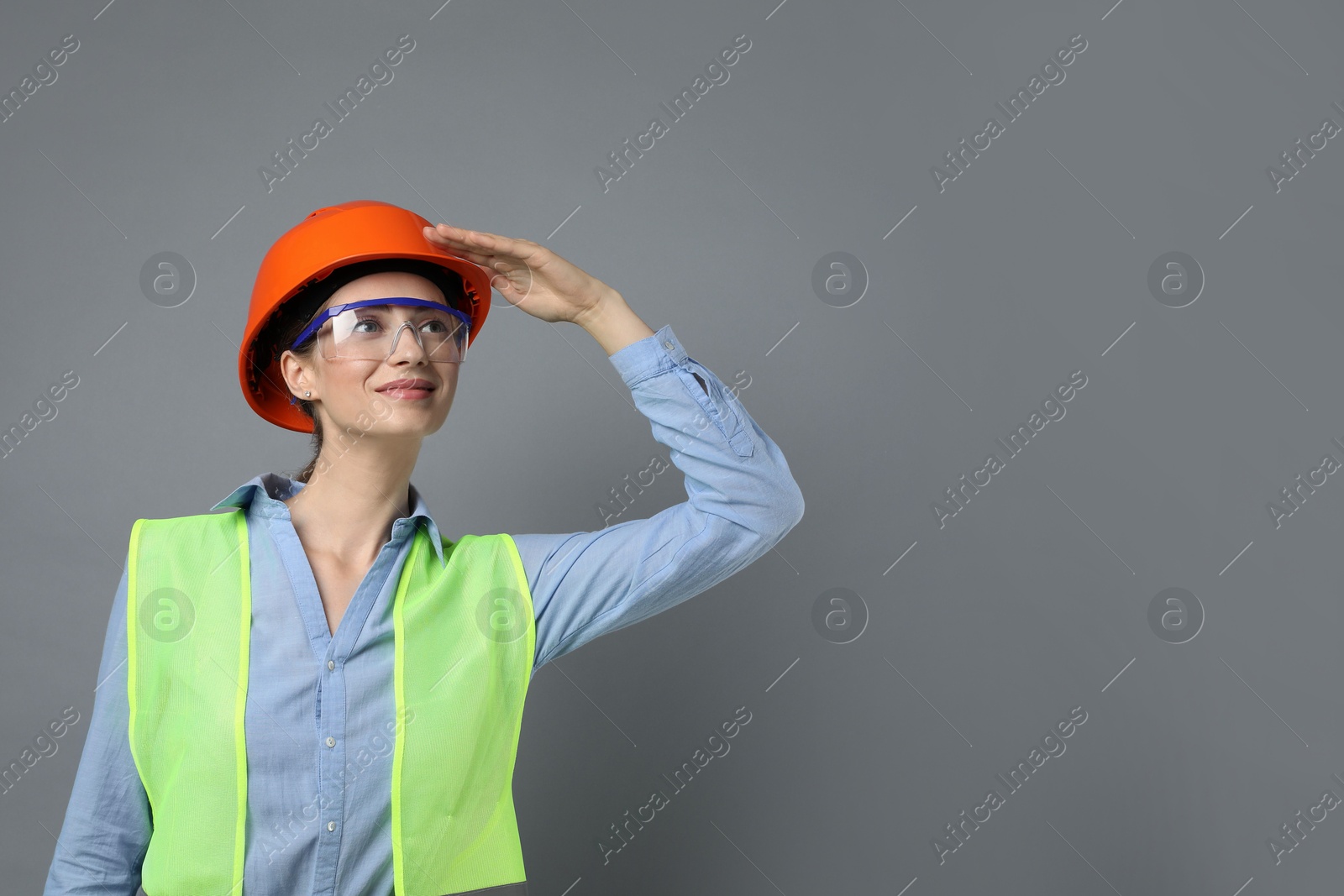 Photo of Engineer in hard hat and goggles on grey background, space for text