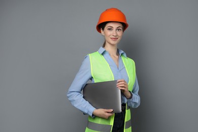 Engineer in hard hat with laptop on grey background, space for text