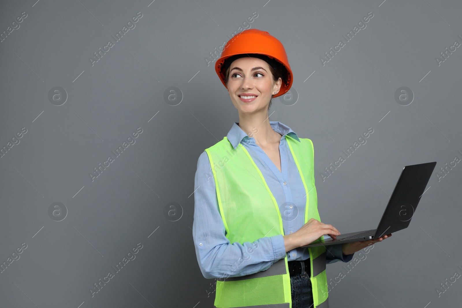 Photo of Engineer in hard hat with laptop on grey background, space for text